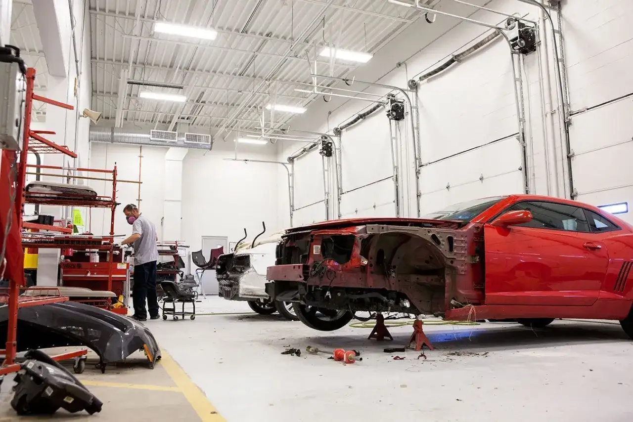 Taller mecánico con coches en reparación. Un mecánico trabaja en un coche rojo sin motor. Averigua cuanto cuesta cambiar el motor de un coche.