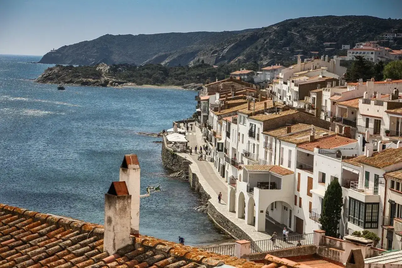 Vitt hus längs kusten vid Costa Brava, med blått hav och gröna kullar i bakgrunden.