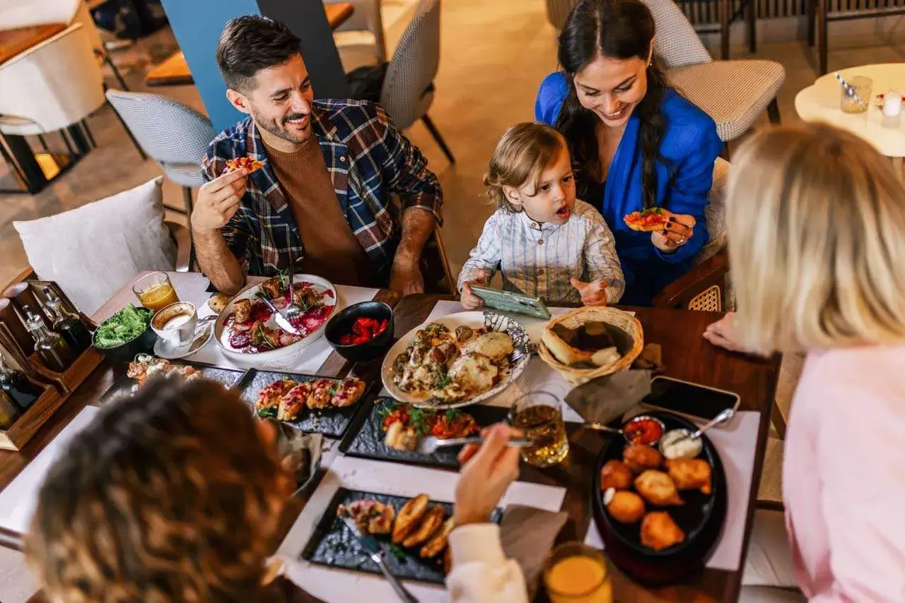 Rodzina cieszy się pysznym posiłkiem w restauracji z wyróżnieniem Bib Gourmand. Na stole różnorodne dania, od przystawek po dania główne.