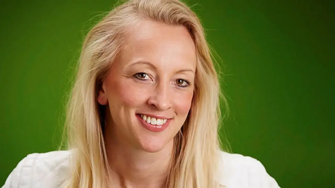 Anna Wikland ler glatt mot kameran, med sitt blonda hår och vita jacka mot en grön bakgrund.