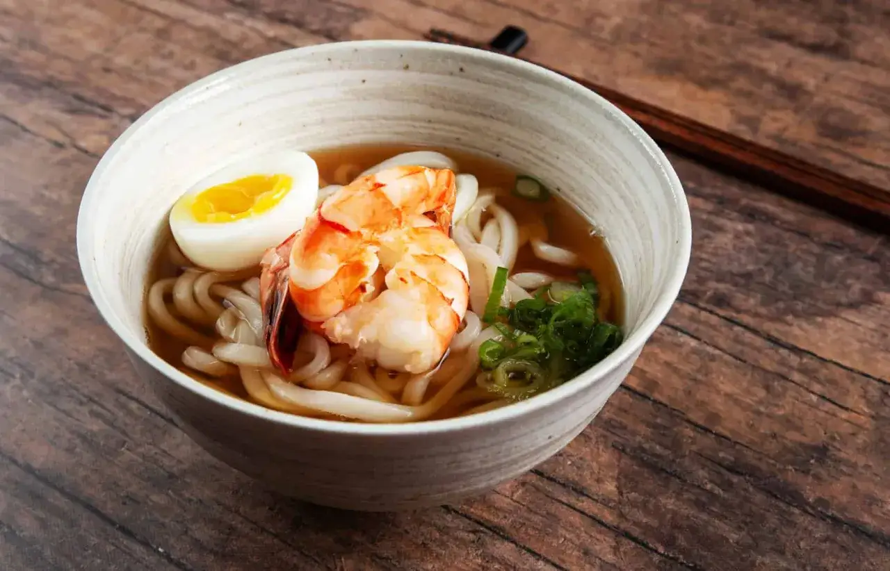 Miseczka z grubym makaronem udon, krewetkami, jajkiem i szczypiorkiem. Pyszne danie, które rozgrzewa.