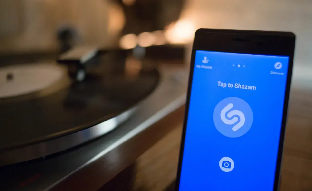 Telefon z aplikacją Shazam gotowy do rozpoznawania muzyki. Obok gramofon z płytą winylową.