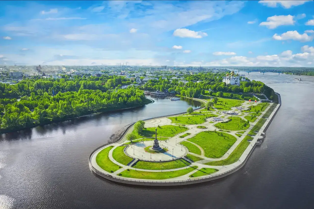 Malowniczy widok na rzekę Wołgę z zielonym parkiem, pomnikiem i cerkwią w oddali.