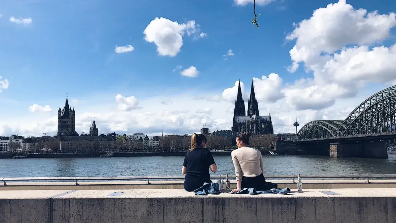 Zwei Frauen genießen den Ausblick auf die Kölner Skyline von einer Rooftop Bar. Dom und Hohenzollernbrücke im Hintergrund.