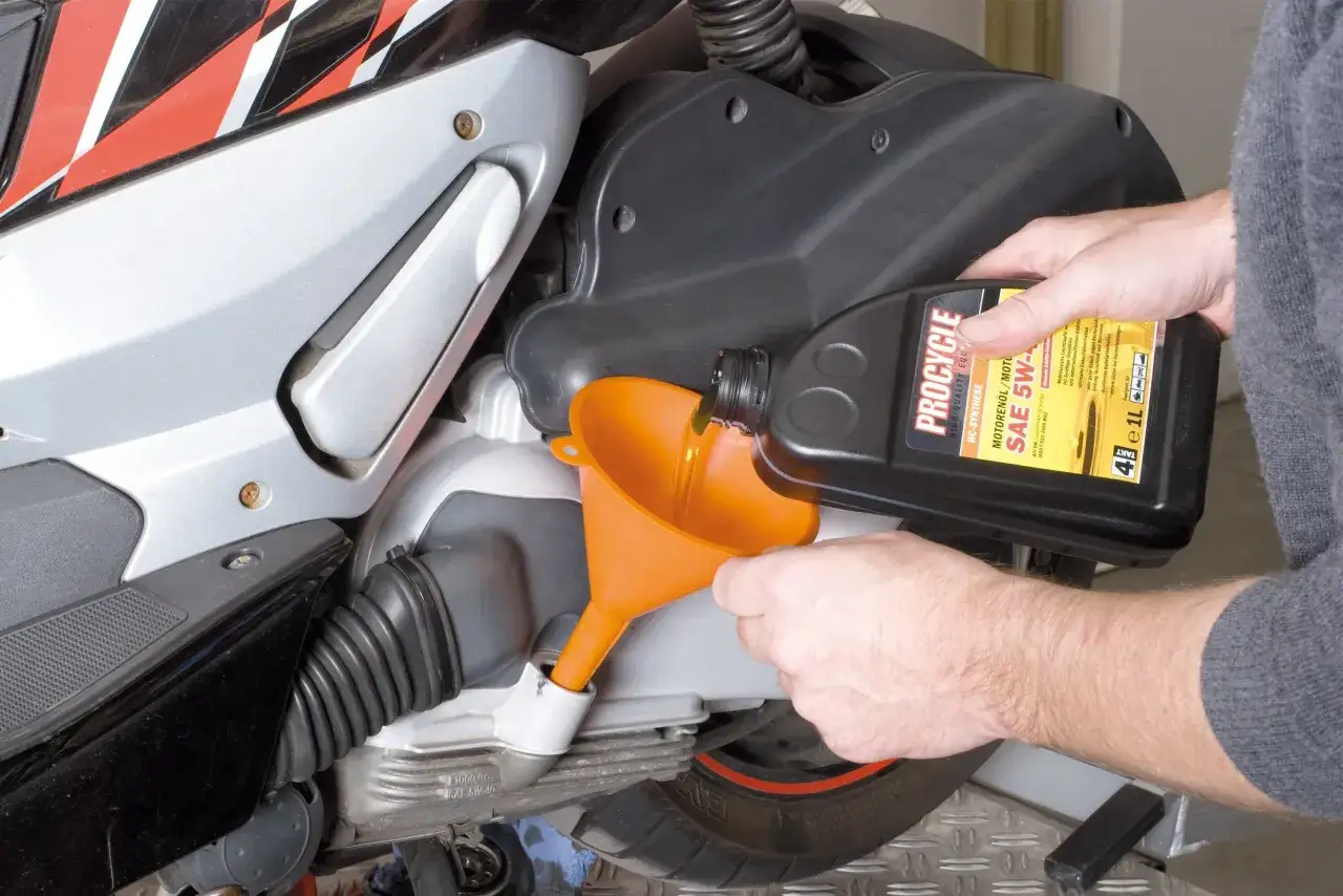 Cambio olio scooter 125 ogni quanto? Un uomo versa olio motore in un imbuto arancione collegato allo scooter.