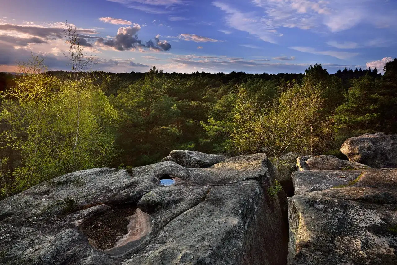 Vue panoramique des gorges de Franchard au coucher du soleil, avec des rochers imposants au premier plan et une forêt dense à perte de vue.