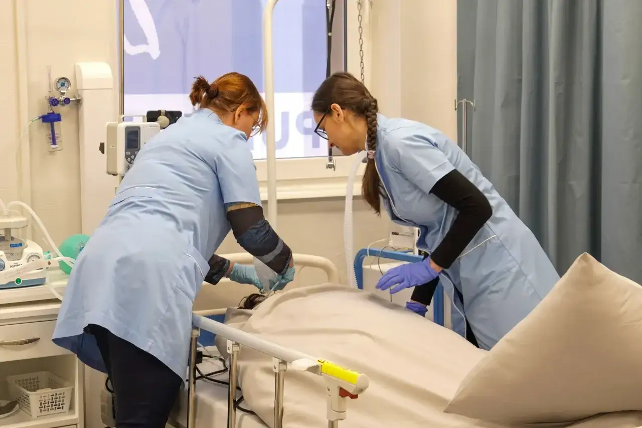 Dwie pielęgniarki przy łóżku pacjenta. Zastanawiasz się, ile trwają studia pielęgniarskie? To praktyczne doświadczenie pokazuje ich pracę.