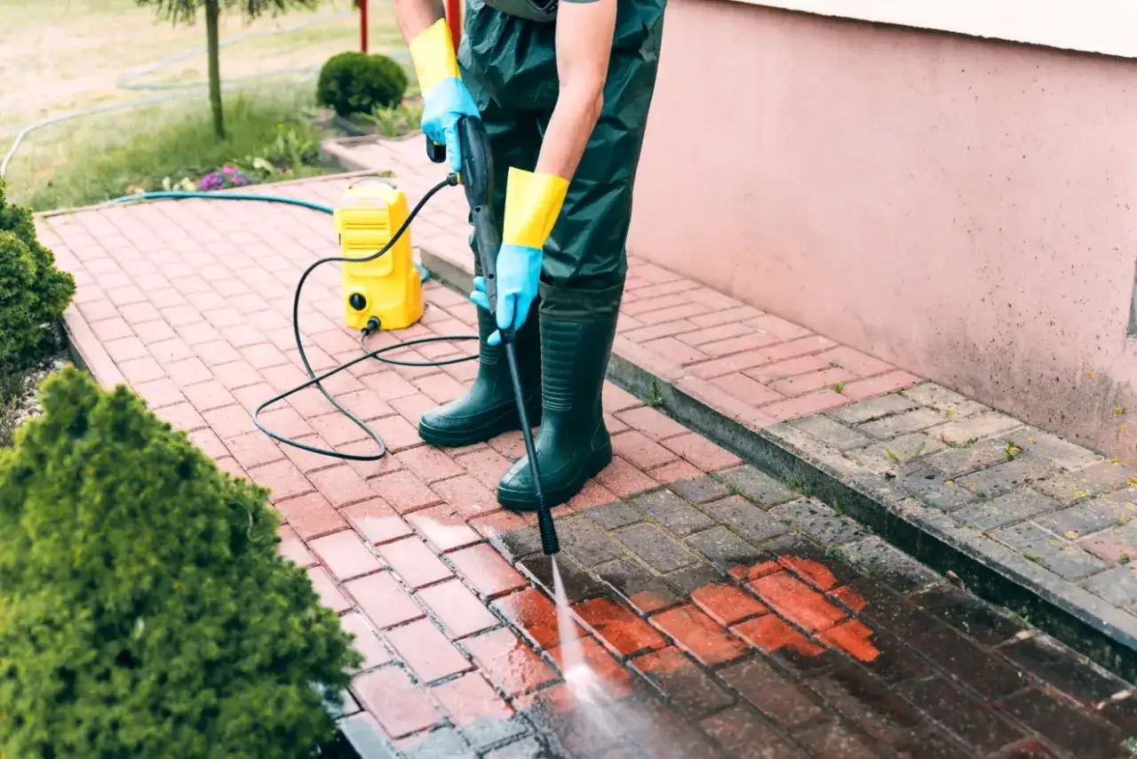 Husmorstips för att ta bort mossa på stenplattor: en person med högtryckstvätt rengör en uteplats.