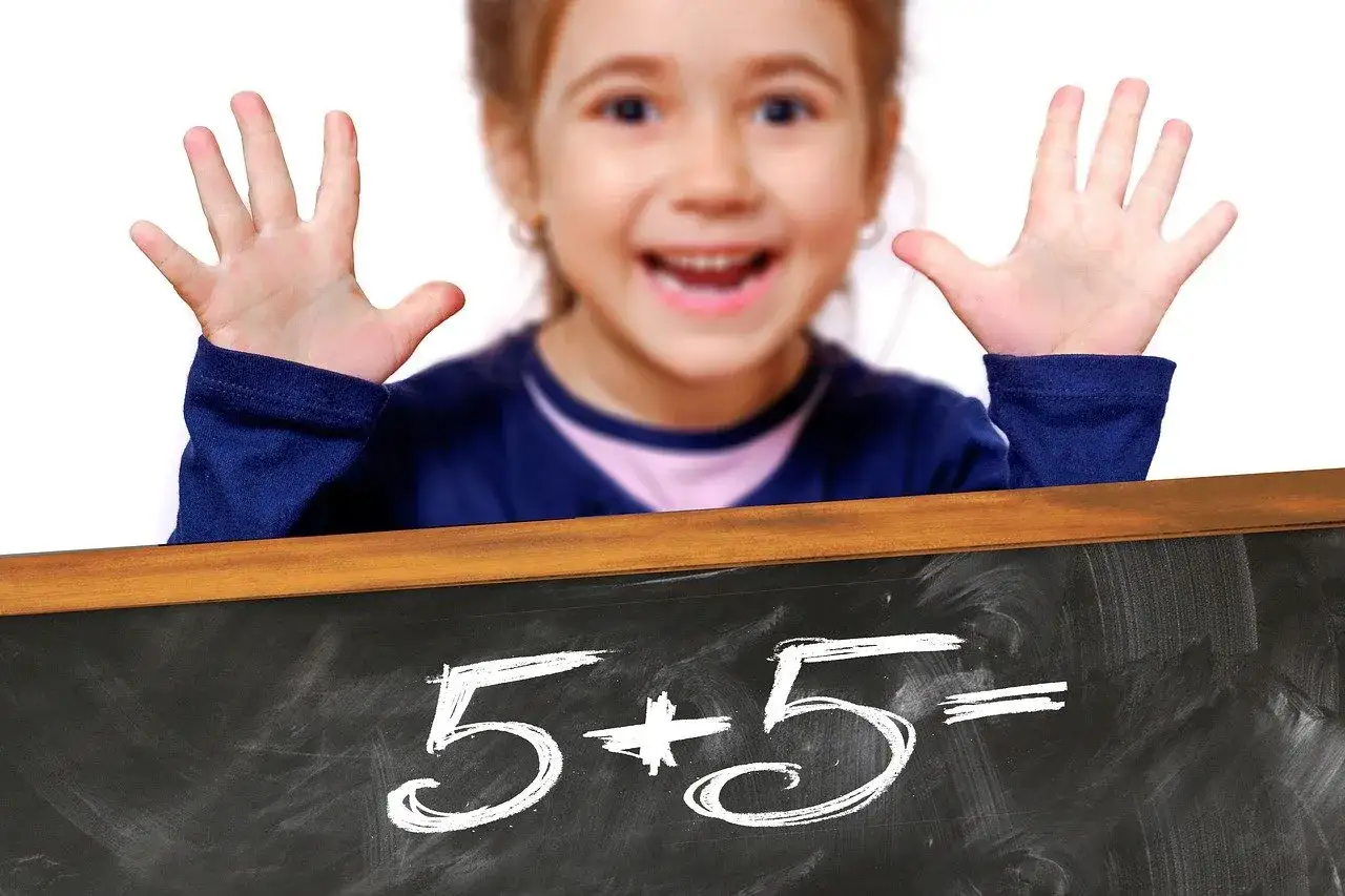 Niña feliz muestra sus manos, lista para el repaso de matemáticas de 2 primaria. En la pizarra, 5+5=.