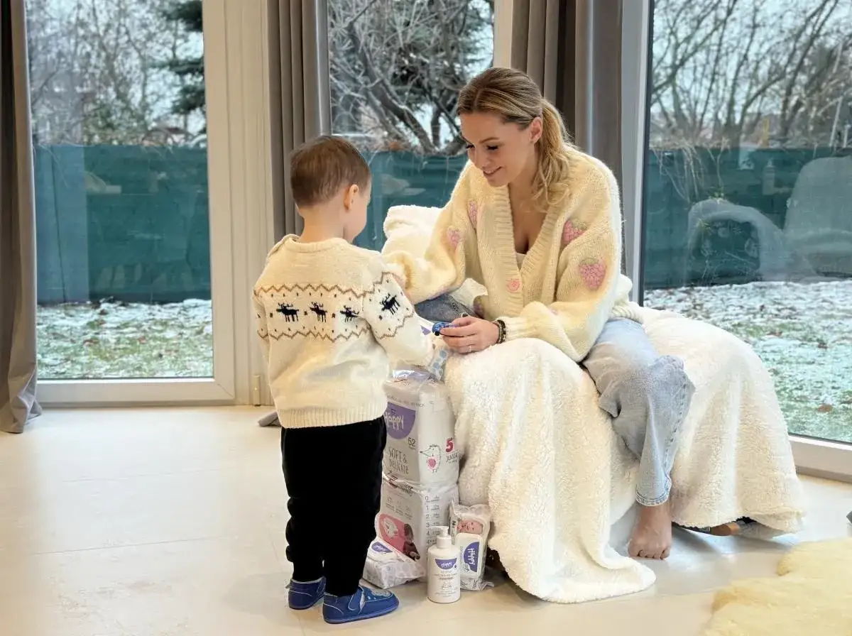 Agnieszka Hyży z dziećmi przygotowuje zapasy. Uśmiechnięta mama i synek przy stosie pieluch i kosmetyków.