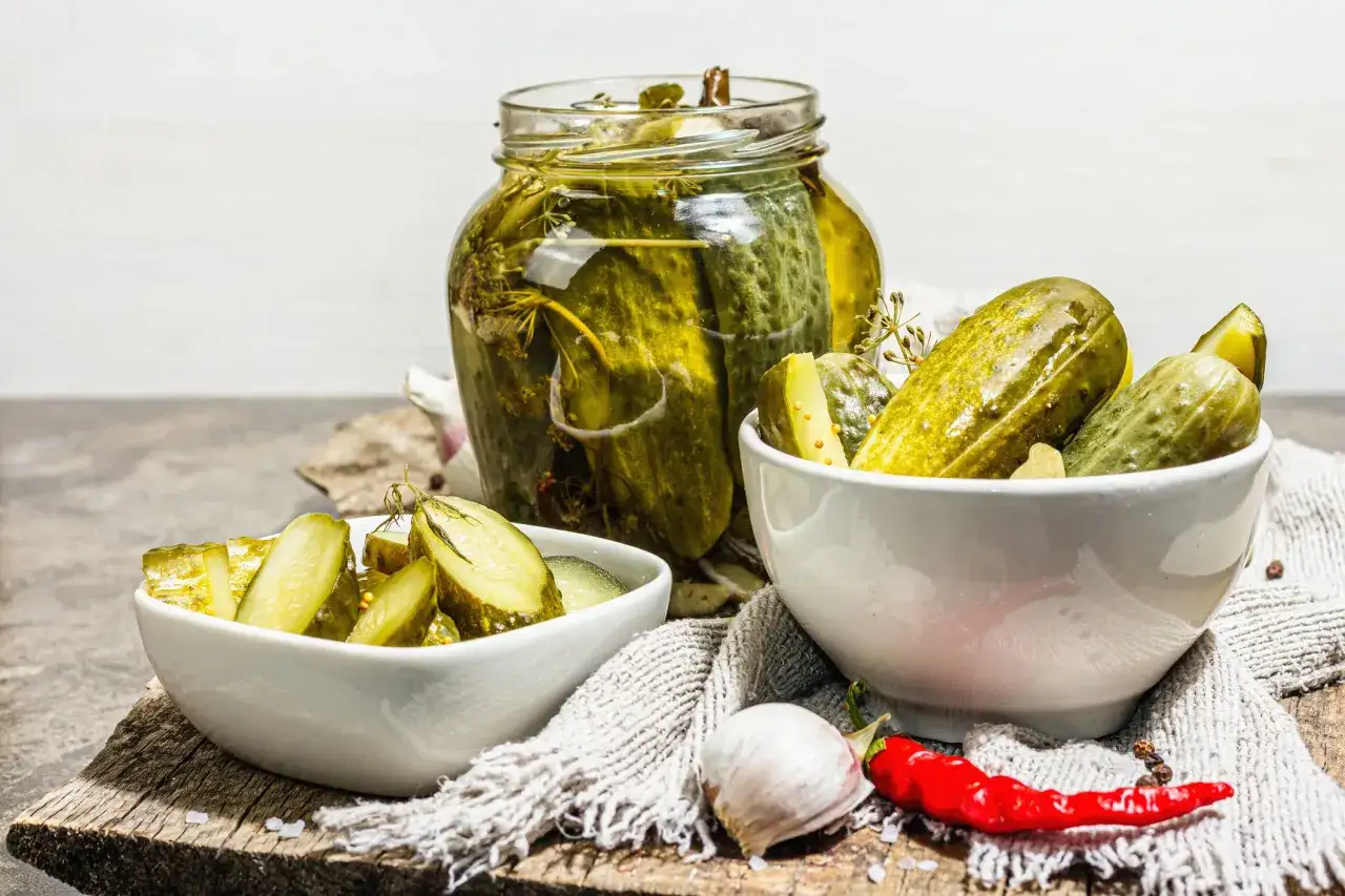 Cetrioli in agrodolce in un barattolo e ciotole, con aglio e peperoncino.