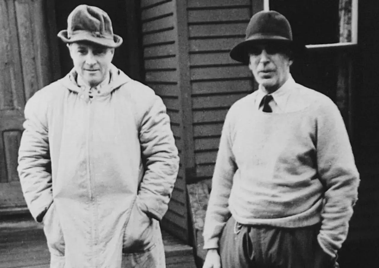 Two men in hats stand outside. The man on the left wears a long coat, the man on the right a sweater. Perhaps these are the founders of Morgan Stanley.