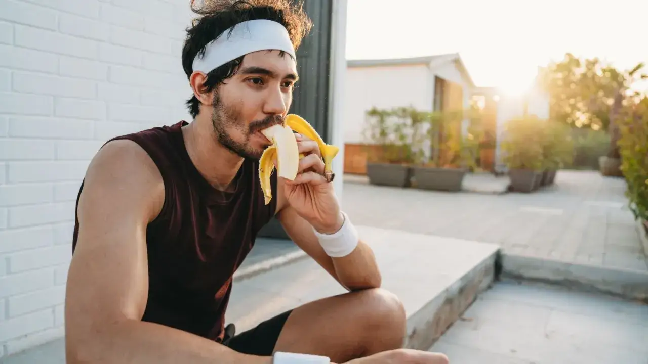 Atleta mangia una banana, un esempio di cosa sono i carboidrati per recuperare energie dopo l'allenamento.