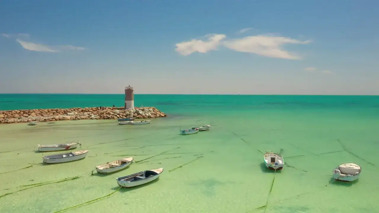 Djerba na co uważać? Spokojne morze, łodzie kołyszące się na wodzie i latarnia morska. Uważaj na słońce i ciesz się widokiem!