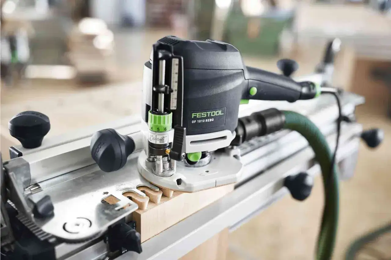 La défonceuse Festool OF 1010 REBQ-plus, avec son guide, crée des entailles précises sur une pièce de bois.