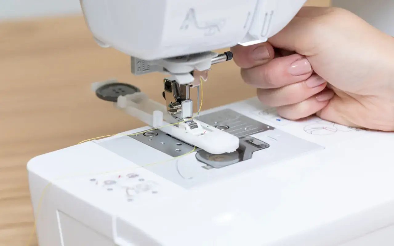 Main d'une personne utilisant un pied-de-biche pour apprendre comment faire une boutonnière sur une machine à coudre.