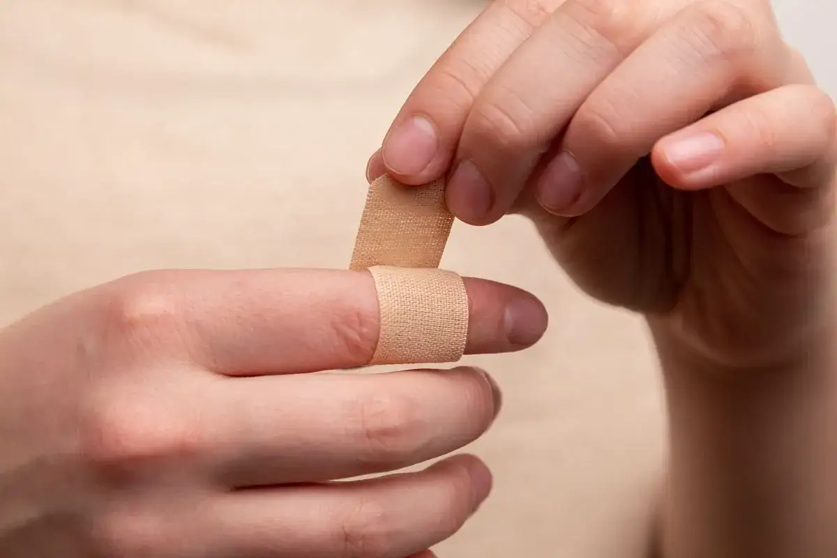 Dłoń zakłada plaster na zraniony palec, łagodząc b&oacute;l i cierpienie.
