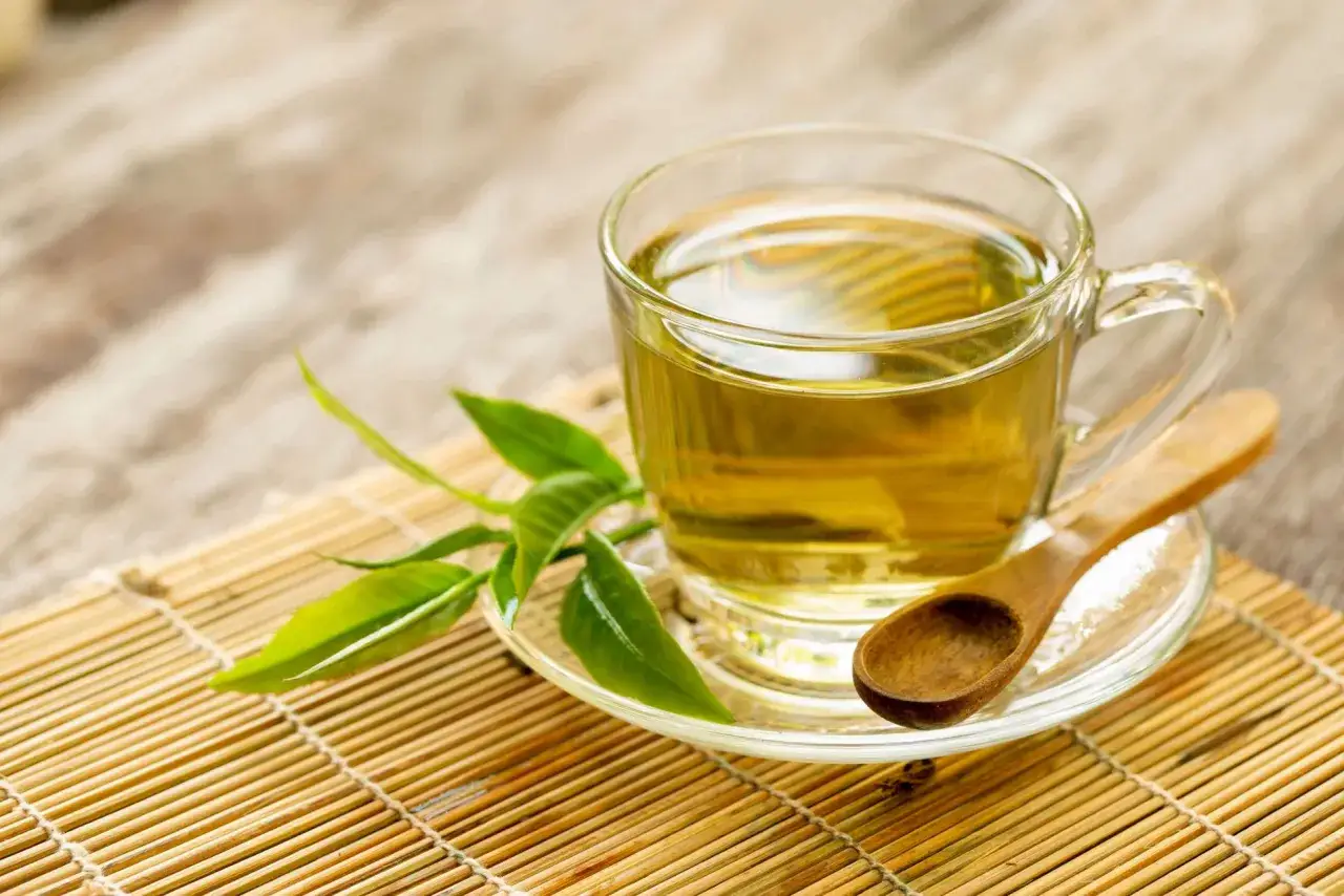 Une tasse de tisane verveine dorée, avec des feuilles fraîches et une cuillère en bois sur un tapis de bambou.