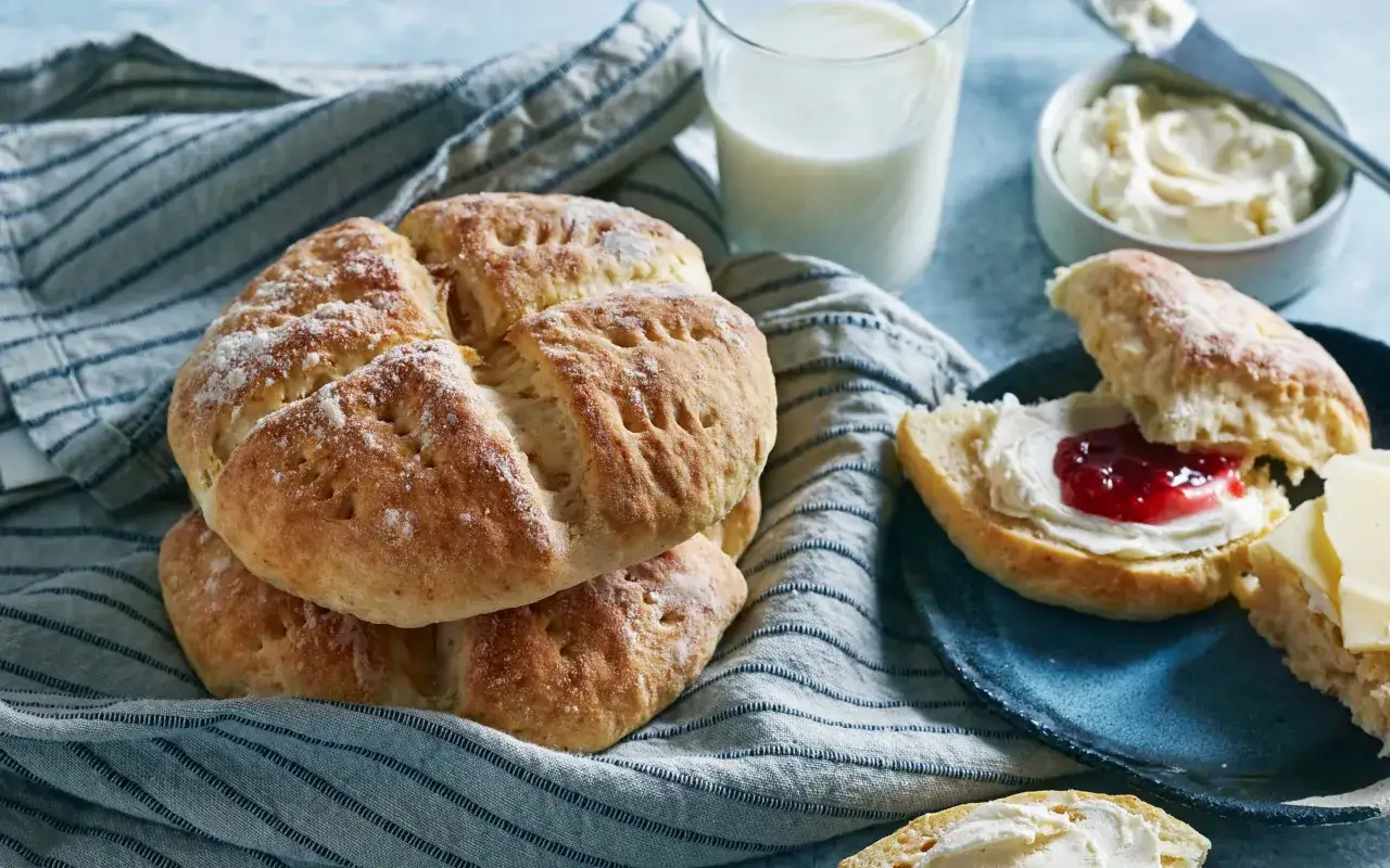 Nybakade scones med keso och sylt, redo att avnjutas med ett glas mjölk.