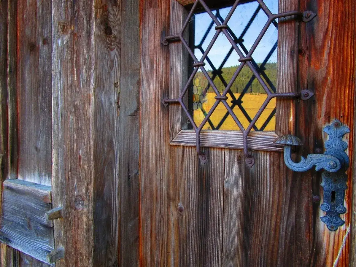 Maniglia antica su porta di legno. Un piccolo oblò con inferriata mostra un paesaggio. Come avvitare una vite che gira a vuoto nel legno?