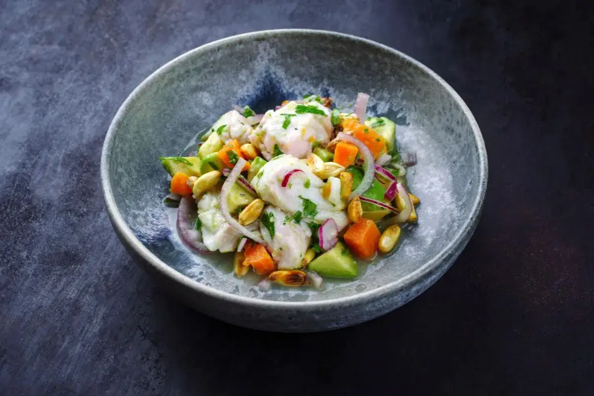 Un ceviche frais et coloré, parfait pour une recette d'été. Poisson blanc, avocat, oignon rouge, maïs et coriandre dans un bol.