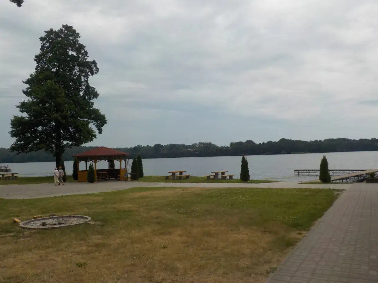 Nad jeziorem, w miejscu zwanym kamień krajeński, stoi altana, a obok niej ławki i stoły. W oddali widać las.