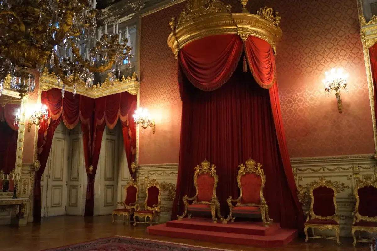 Prunkvoller Thronsaal im Lissabon Palast mit roten Samtthronen, goldenen Verzierungen und schweren Vorhängen.