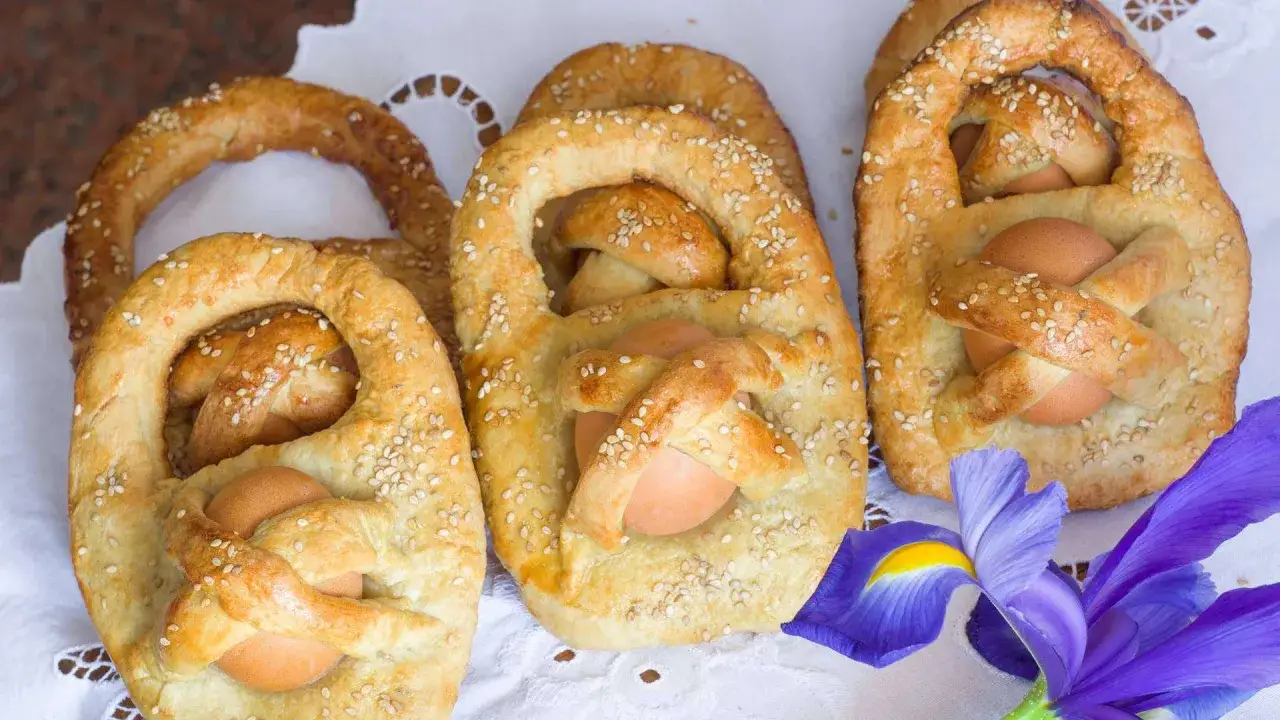 Dolci cestini di pane con uova, decorati con semi di sesamo, tipici della **Pasqua in Sicilia**. Un fiore viola completa la scena.