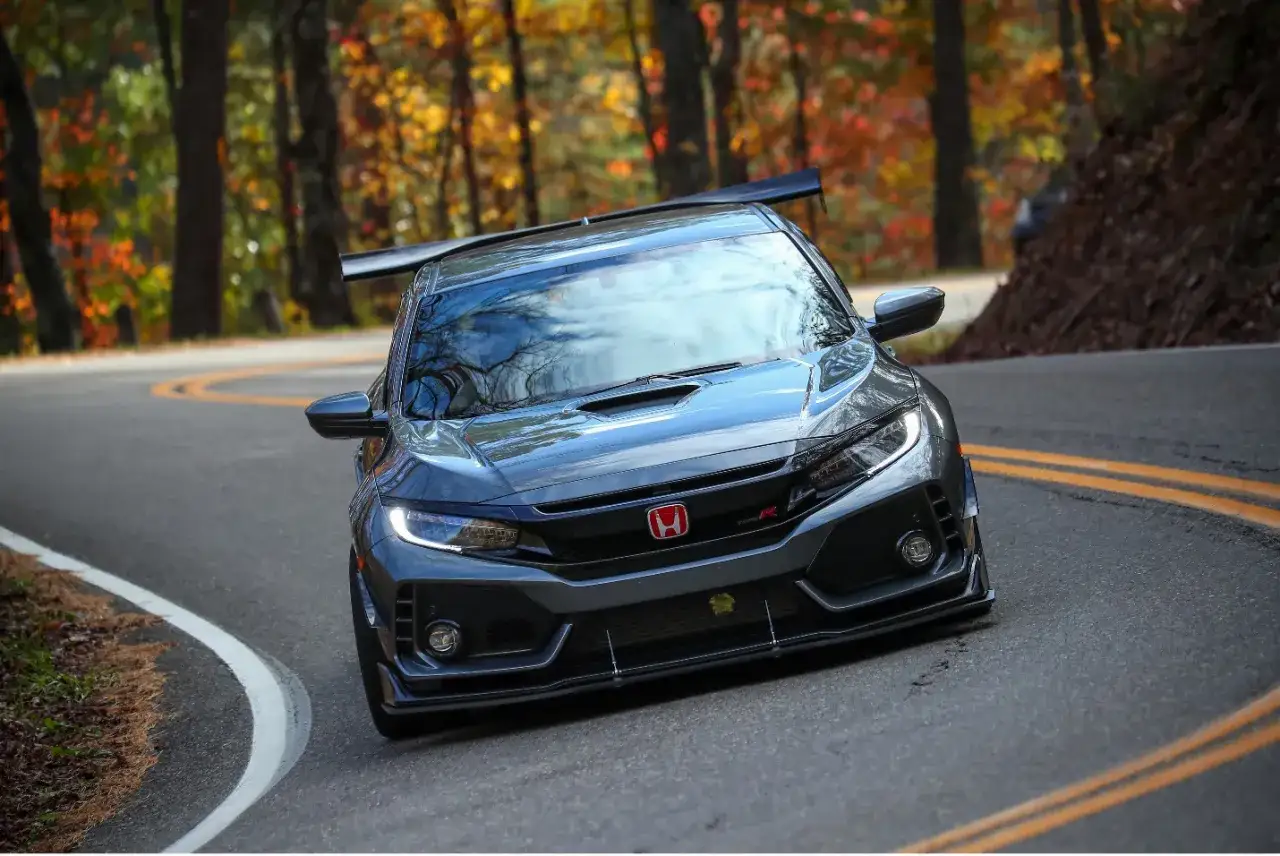 Ein dunkler Honda Civic Type R 2018 fährt auf einer kurvigen Straße durch einen bunten Herbstwald.