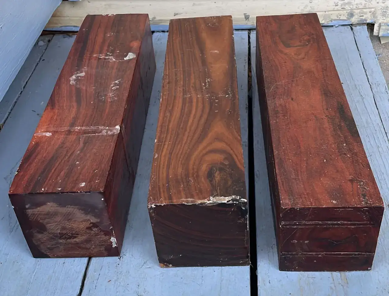 Tres bloques de madera de palisandro con vetas oscuras y rojizas, listos para ser tallados.