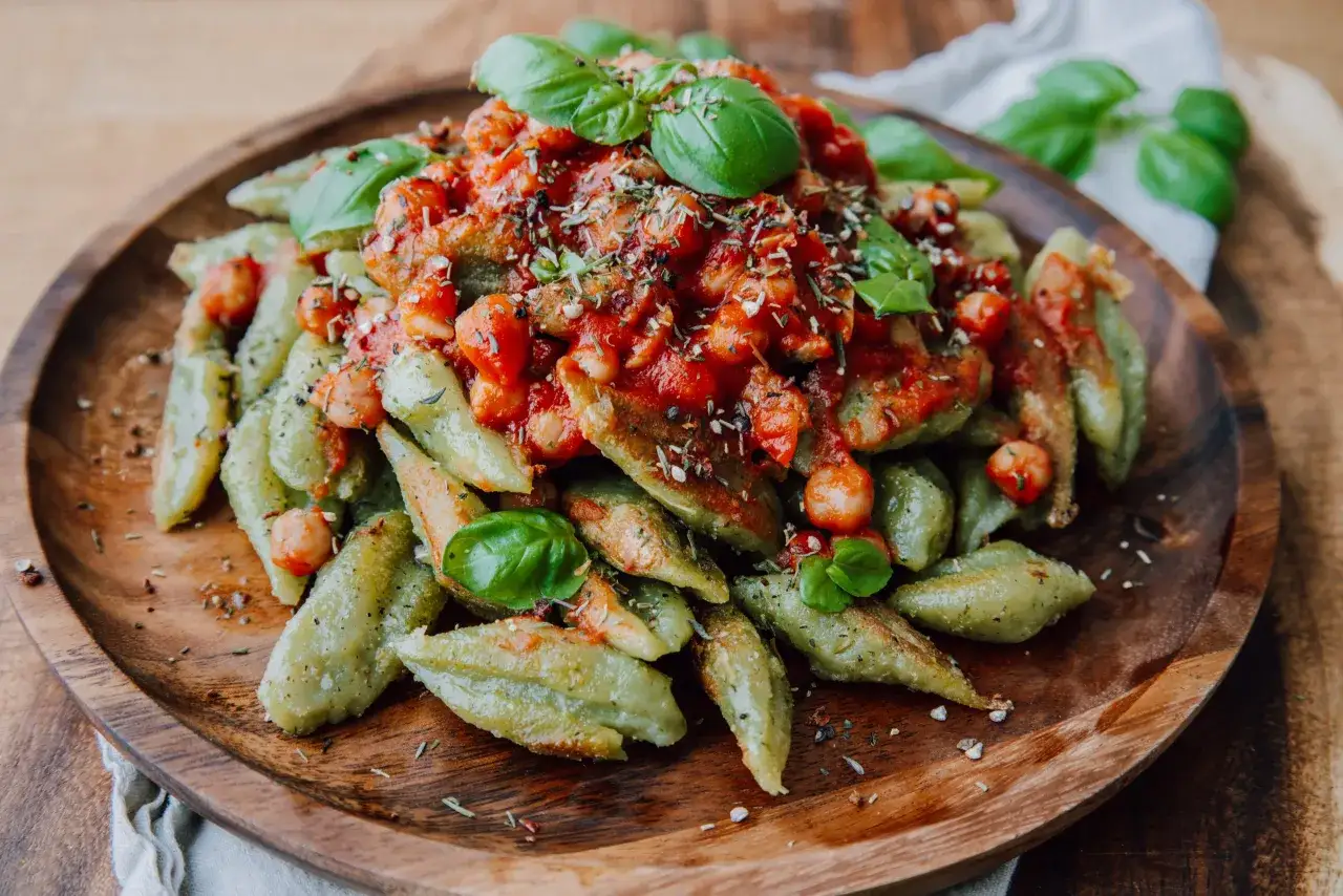 Macarrones con brócoli, cubiertos con salsa de tomate y garbanzos, adornados con hojas de albahaca fresca. Un plato vibrante y saludable.