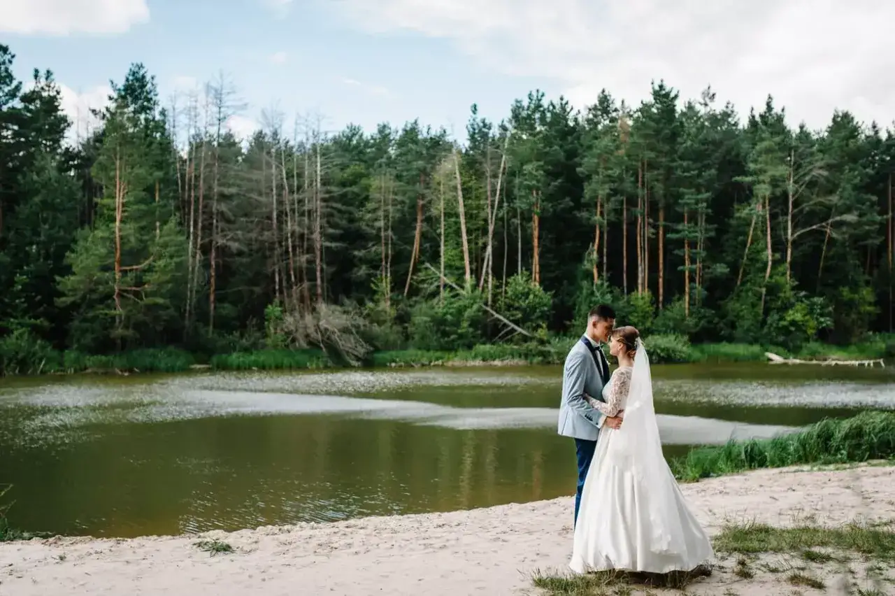 Ein Brautpaar genießt den Moment am Ufer eines Sees. Die Hochzeit am See ist von einem dichten Wald umgeben.