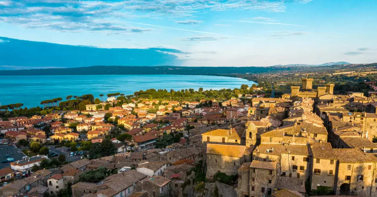 Vista aerea di un borgo medievale con castello, affacciato su un lago azzurro. Perfetto tra i borghi da visitare vicino Bolsena.