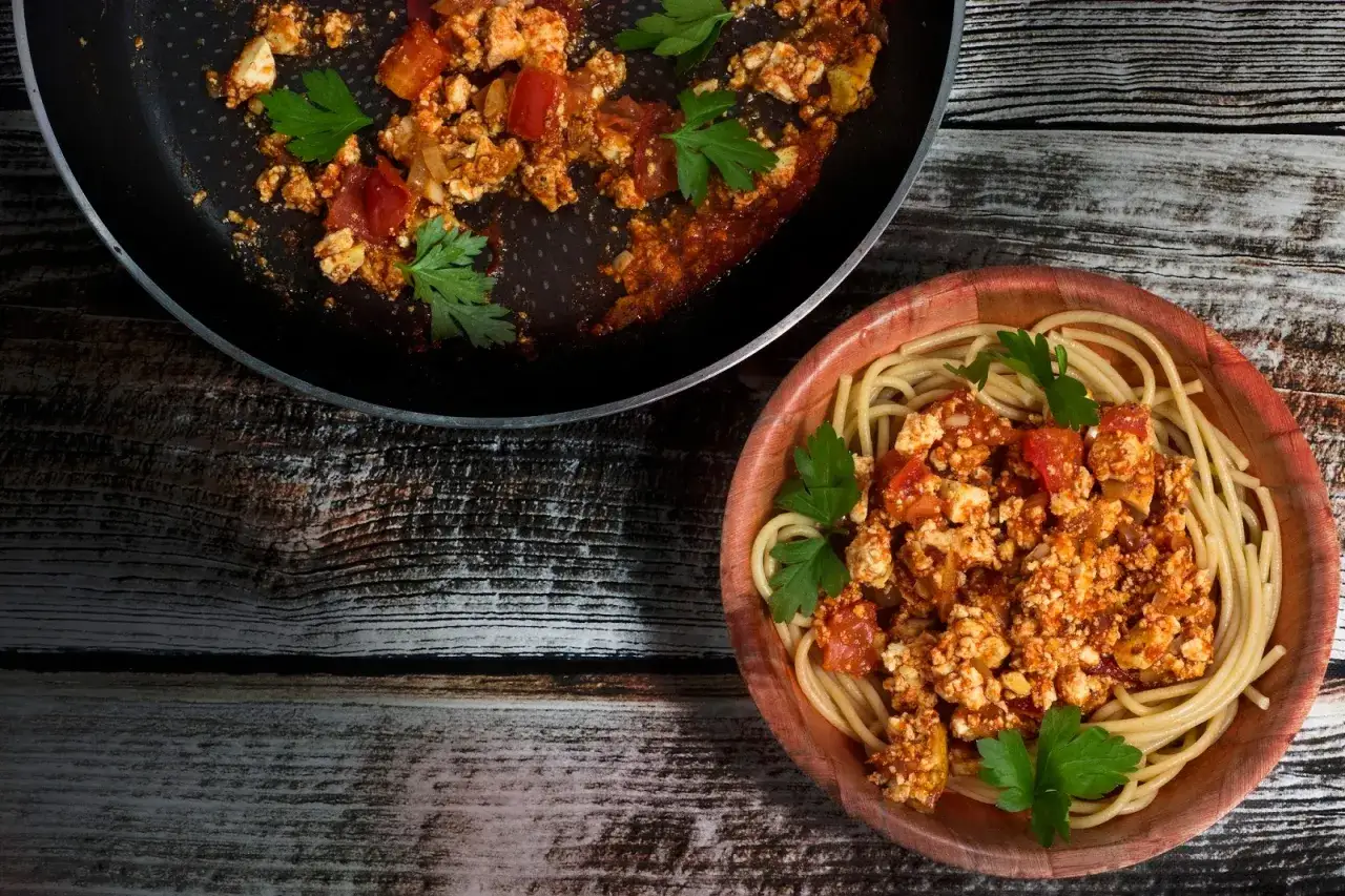 Spaghetti bez mięsa z tofu i pomidorami, udekorowane natką pietruszki, na drewnianym stole.