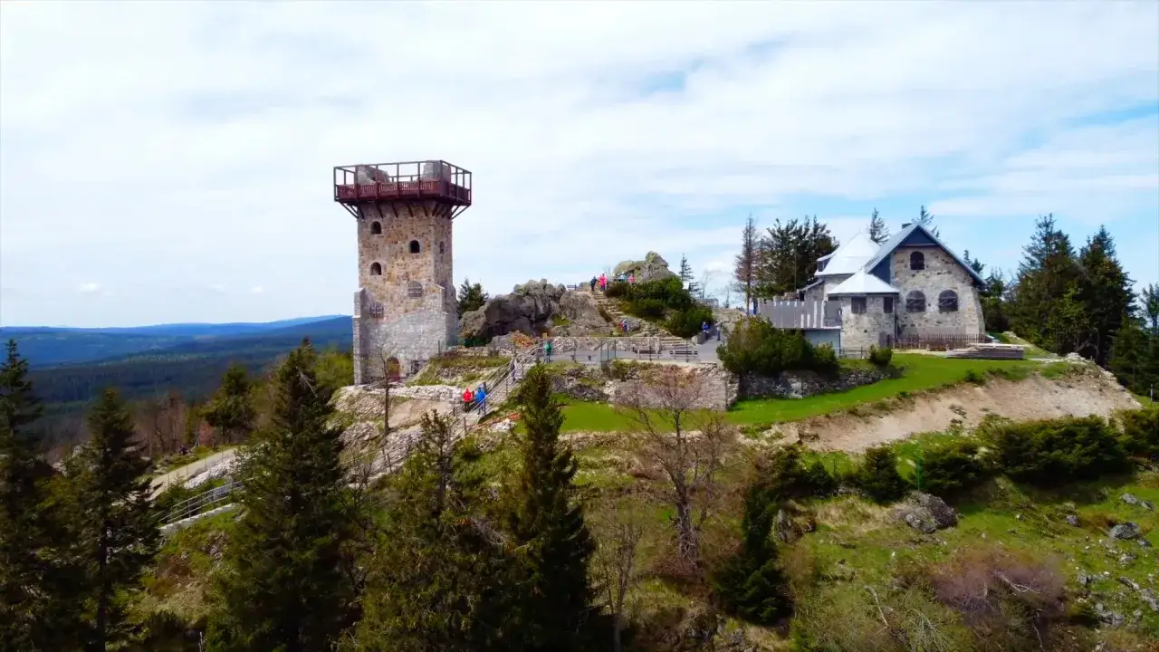 Wysoki kamień, wieża widokowa i kamienny budynek na wzgórzu, otoczone lasem i górami.