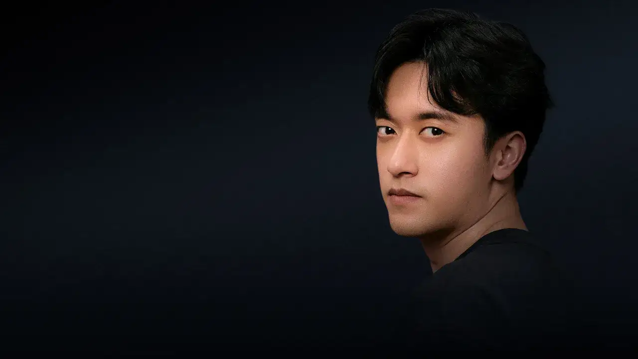 Retrato de Zhou Guanyu, un joven con cabello oscuro y mirada intensa, posando sobre un fondo oscuro.