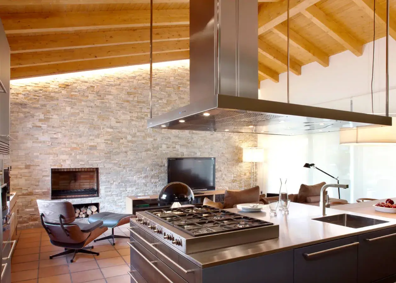 Cocinas de le&ntilde;a modernas con isla central, campana extractora de acero inoxidable y chimenea de piedra.