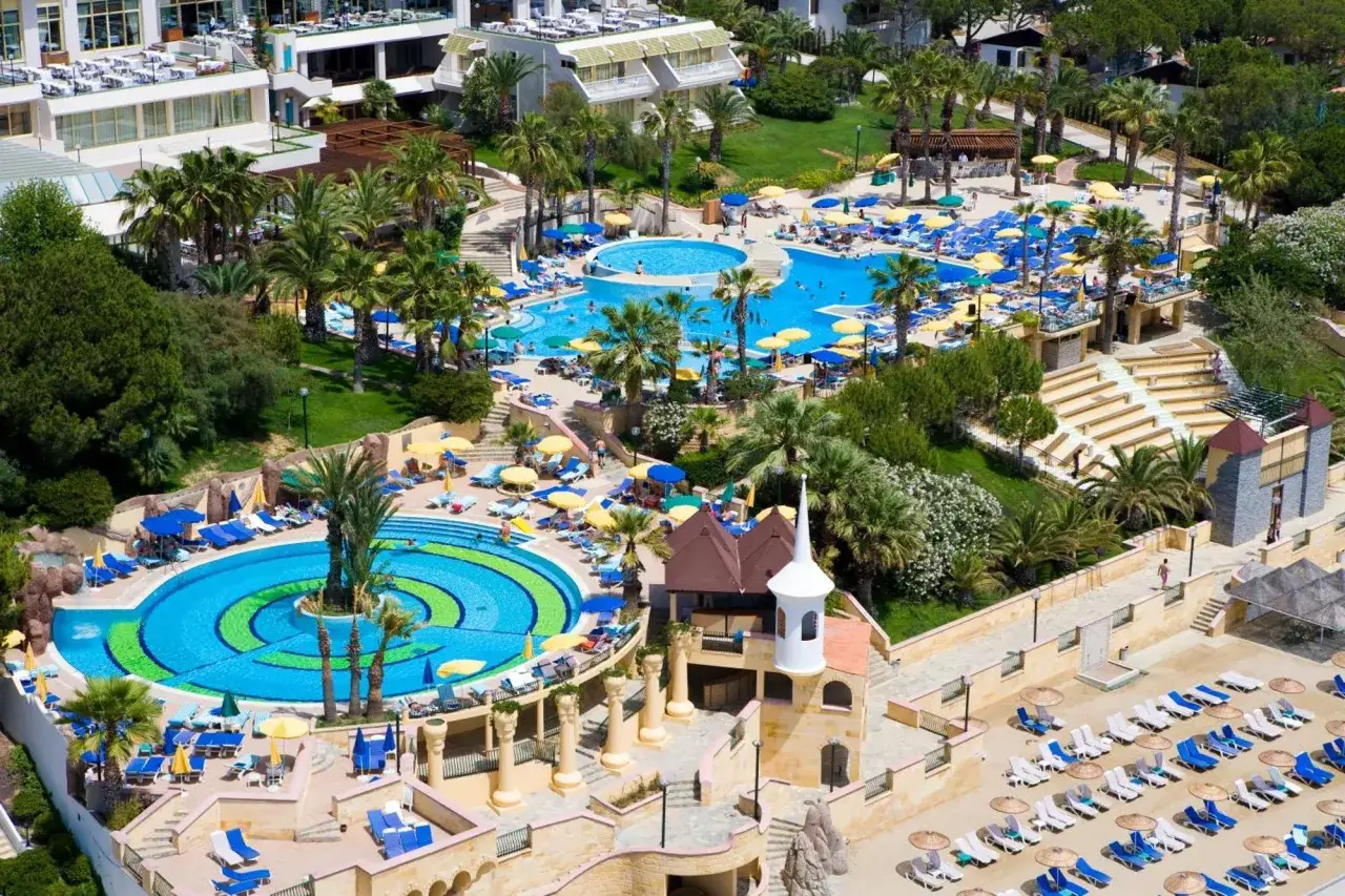 Fantasia de Luxe Kusadasi: luksusowy hotel z basenami, palmami i leżakami na plaży.