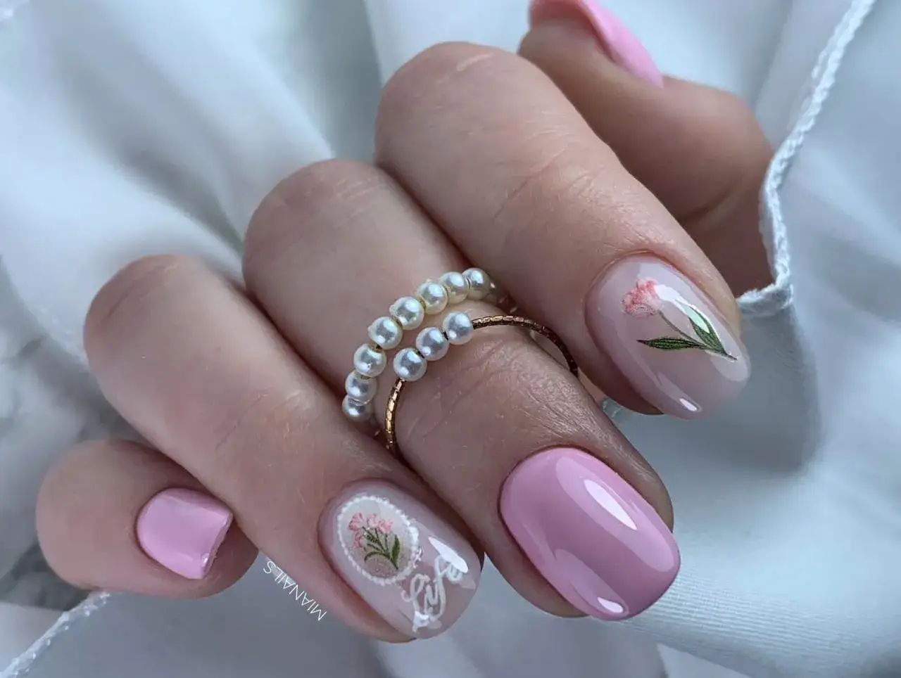 Manicure con colori smalto primavera: rosa cipria e decorazioni floreali delicate, impreziosita da un anello di perle.