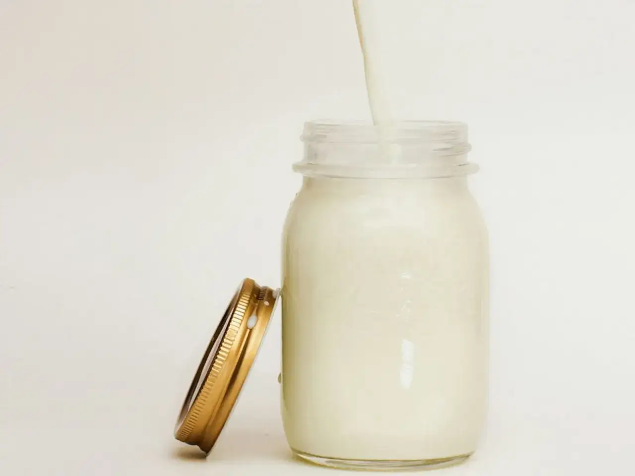Un filet de lait de beurre coule dans un pot en verre, son couvercle dor&eacute; pos&eacute; &agrave; c&ocirc;t&eacute;.