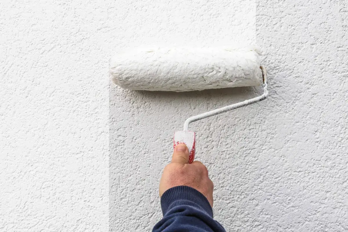 Hand rollt wei&szlig;e Farbe auf eine strukturierte Wand. Die Frage, welche Wandfarbe deckt am besten, wird hier visuell beantwortet.