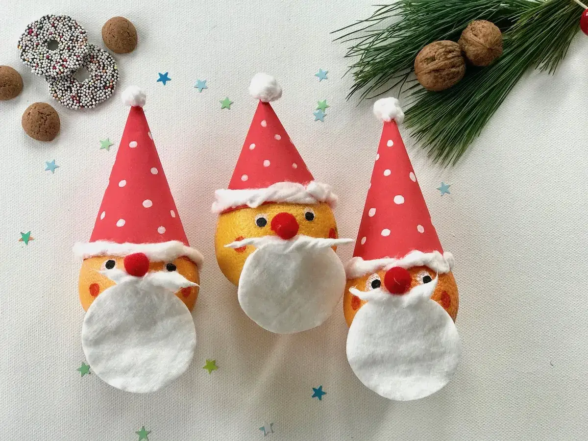 Drei lustige Nikolaus-Gesichter aus Orangen, perfekt für Nikolaus basteln U3. Mit roten Mützen und weißen Bärten.
