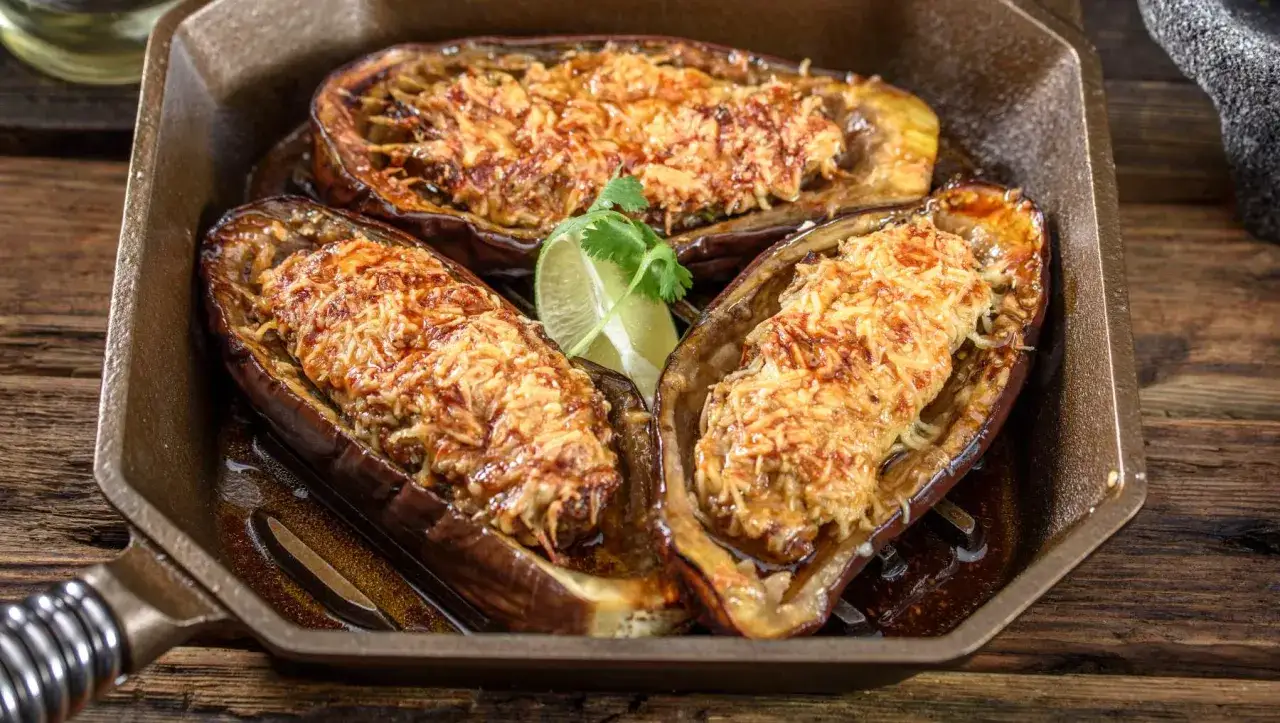 Berenjenas rellenas y gratinadas, cocinadas en airfryer, servidas en una sartén de hierro fundido con un toque de lima.