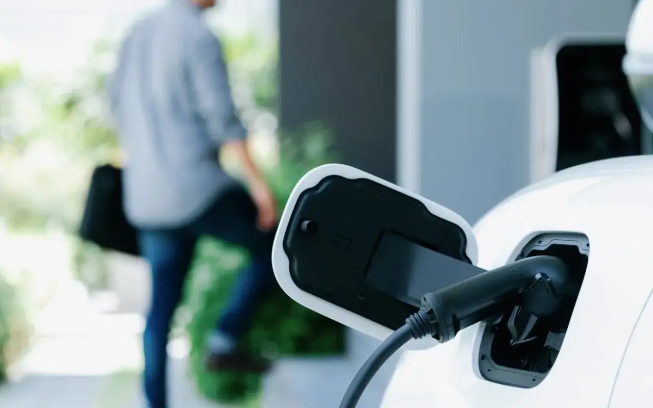 Ładowanie białego samochodu typu plug-in hybrid. Mężczyzna w tle odchodzi od stacji ładowania.