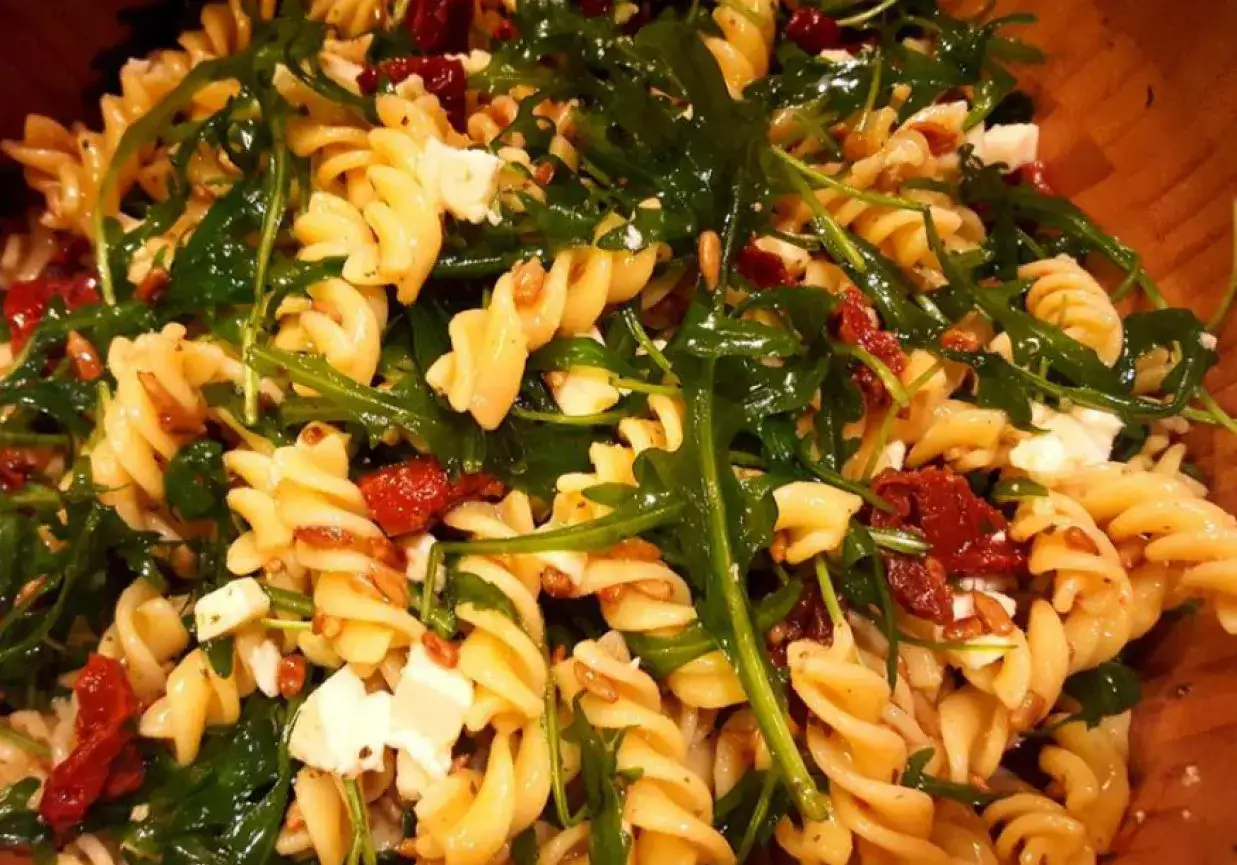 Pyszna sałatka z makaronem fusilli, rukolą, kawałkami sera feta i intensywnymi w smaku suszonymi pomidorami.