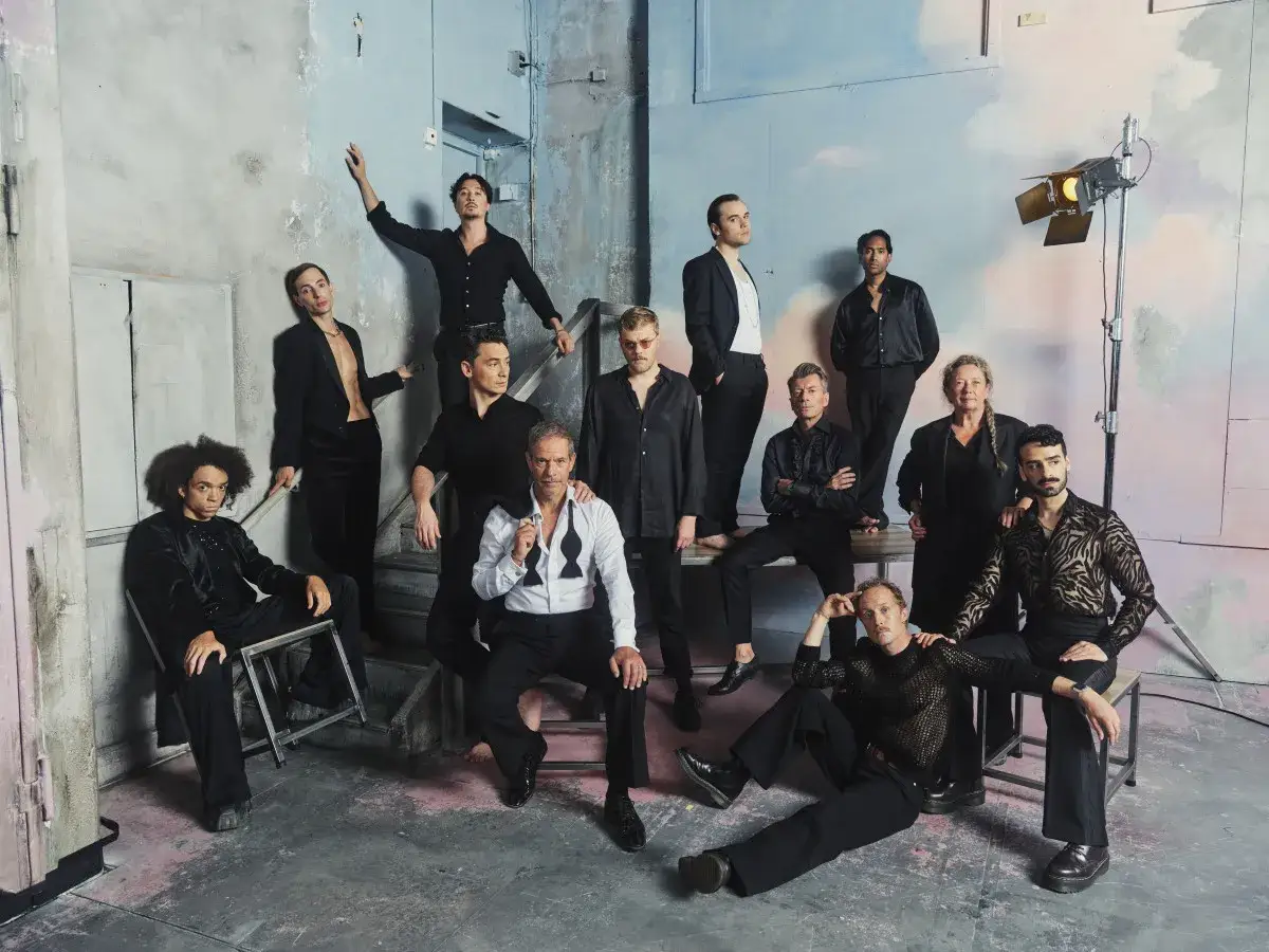 Ensemblen från Dramaten poserar i en konstnärlig miljö. En grupp skådespelare, klädda i svarta kostymer och skjortor, utstrålar en känsla av arv och teaterns magi.