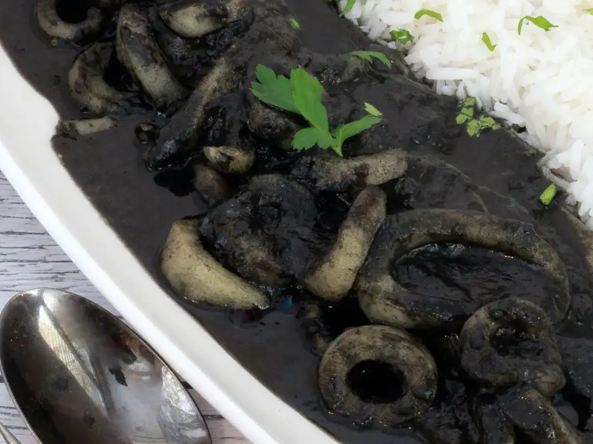 Deliciosos calamares en su tinta, servidos con arroz blanco y perejil fresco. Un plato tradicional lleno de sabor.