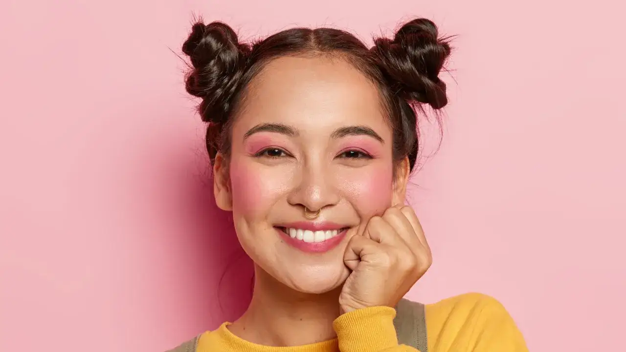 Uśmiechnięta dziewczyna z r&oacute;żowymi cieniami do powiek i rumieńcem, w stylu makeup no makeup.