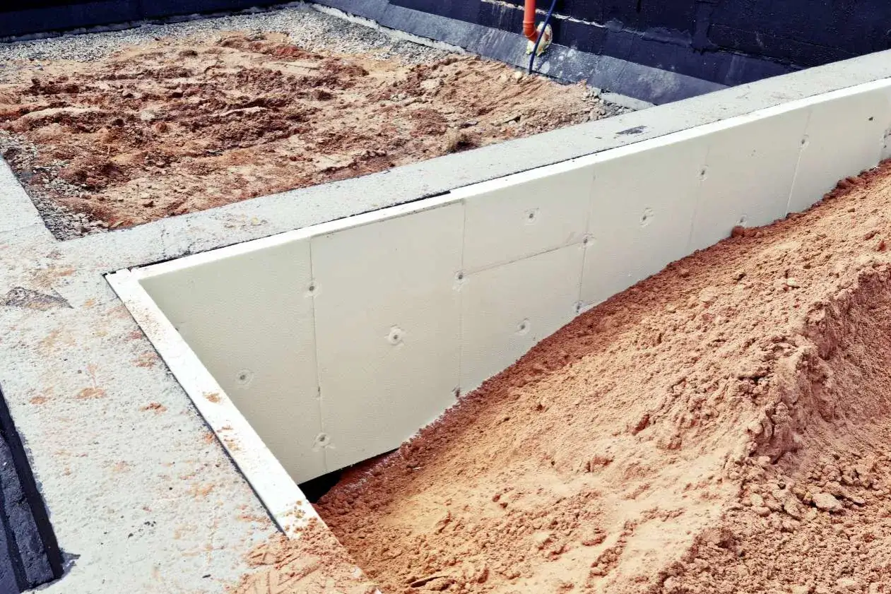 Izolacja fundamentów: biały styropian na ścianach fundamentowych, otoczony piaskiem i żwirem.