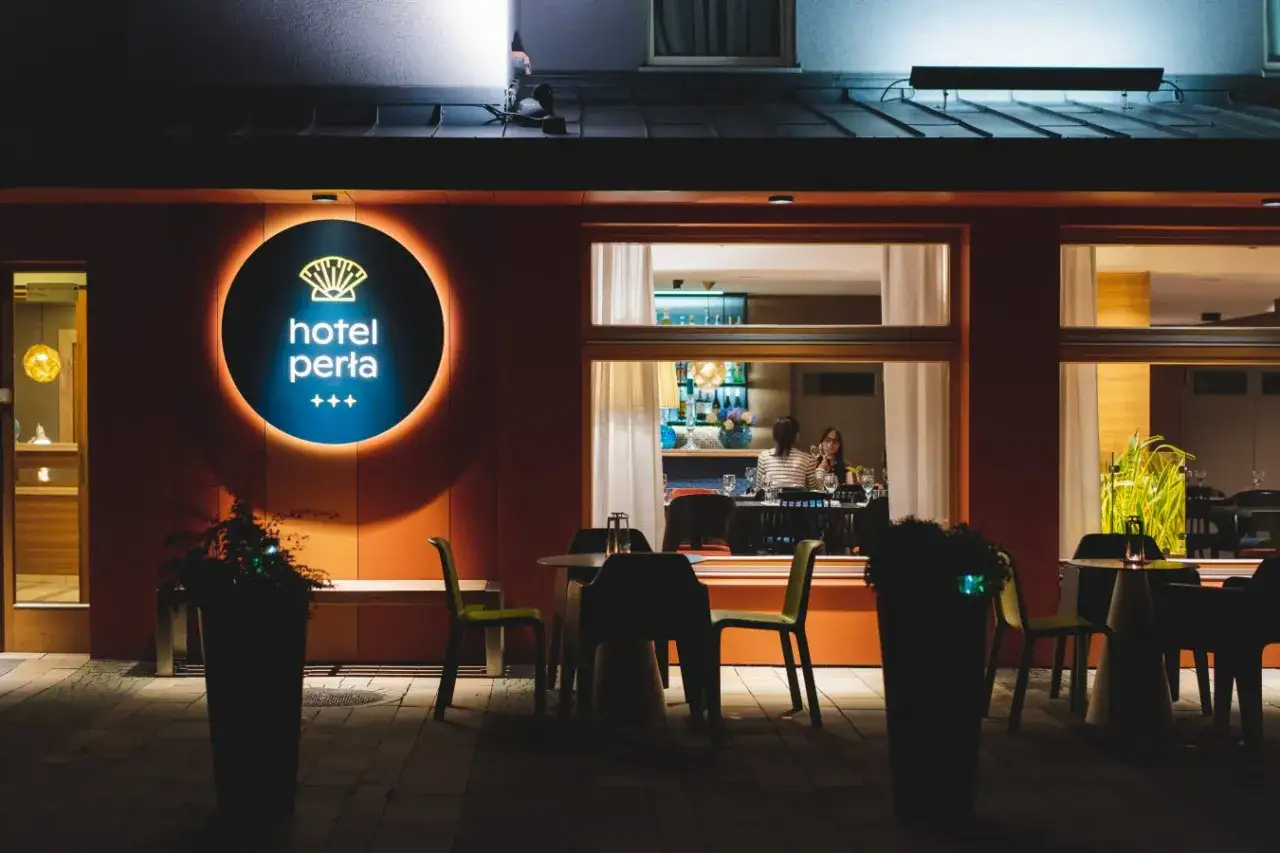 Elegancki hotel Perła Kraków nocą. Wnętrze restauracji z gośćmi, iluminowany neon i stoliki na zewnątrz.